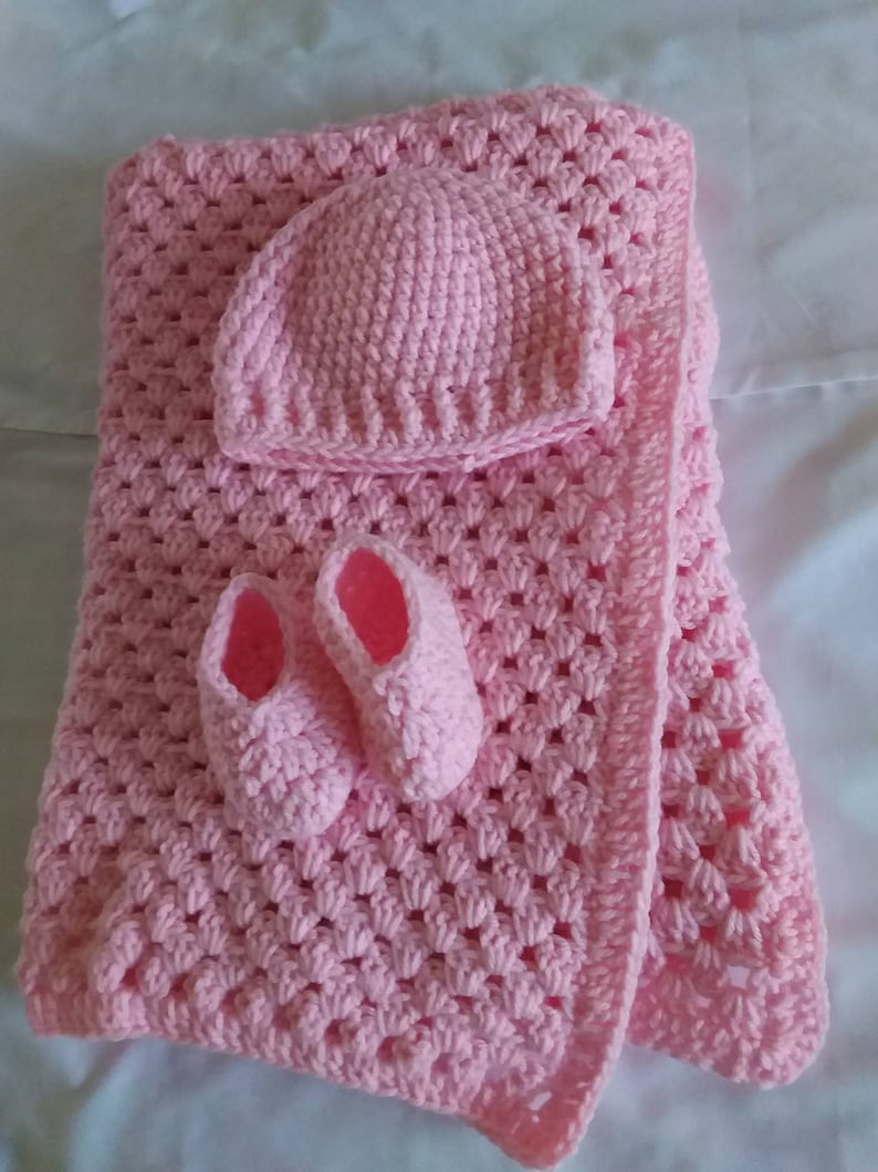 May include: A handmade pink crochet baby set, including a blanket, hat, and booties. The blanket has a textured pattern, and the booties and hat are designed to match. The set is made of soft yarn.