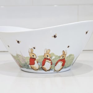 May include: A white ceramic mug with a black handle and the text "But First, Coffee" in a bold, black font. The mug is set against a blurred background, suggesting a cozy setting.