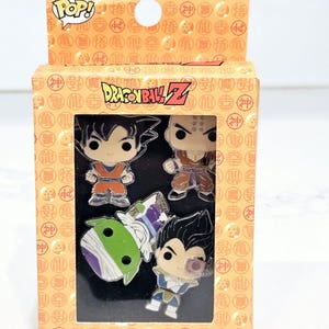 May include: A boxed enamel pin set featuring characters from Dragon Ball Z. The box is orange with the "POP!" logo and "Dragon Ball Z" text. The set includes four character pins with vibrant colors and detailed designs.