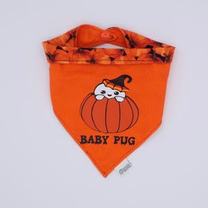 Puede incluir: Bandana naranja para perros con un diseño de calabaza y pug. La bandana presenta un diseño de calabaza con un pug con un sombrero de bruja. El texto "BABY PUG" está impreso debajo. El borde superior tiene un patrón de calabaza.