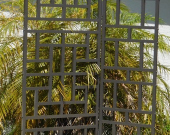 May include: A black metal trellis with a geometric design, standing in front of a green bush.