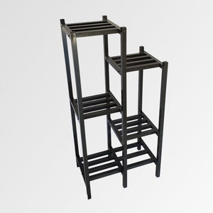 May include: A black, multi-tiered plant stand with a stepped design. The stand has four square platforms of varying heights, each with horizontal slats. The frame is constructed of square metal tubing.