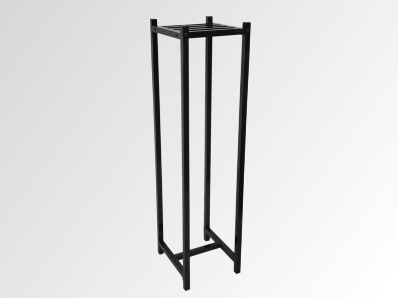 May include: A tall, black metal plant stand with a square top and base. The stand has a rectangular frame with vertical supports and a slatted top. The design is minimalist and modern, suitable for displaying plants or decorative items.
