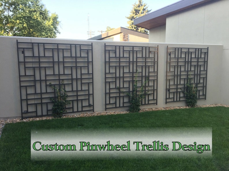 May include: Three black metal pinwheel trellis designs mounted on a light gray wall. The trellis has a geometric pattern and is placed in a garden setting with green grass and small plants. The text "Custom Pinwheel Trellis Design" is at the bottom.