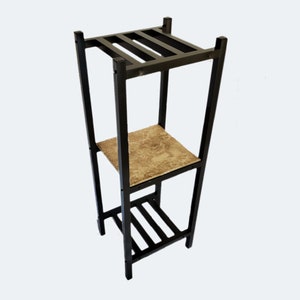May include: A black metal plant stand with three levels. The top and bottom levels have a slatted design, while the middle shelf features a patterned, beige surface. The stand is designed to hold plants or decorative items.