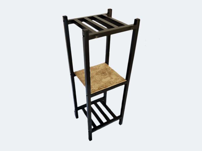 May include: A black metal plant stand with three levels. The top and bottom levels have a slatted design, while the middle shelf features a patterned, beige surface. The stand is designed to hold plants or decorative items.
