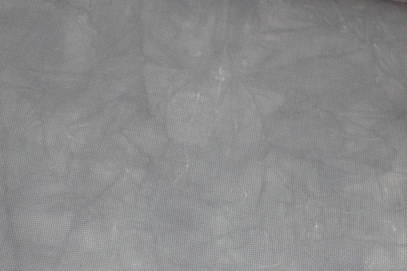 May include: A close-up of a plain, light gray fabric with a subtle woven texture. The fabric has a slightly wrinkled appearance.