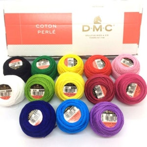May include: A collection of colorful DMC Coton Perlé embroidery thread balls in various shades, including black, green, yellow, red, pink, and purple. The threads are neatly arranged in front of a box with the DMC logo and "Coton Perlé" text.
