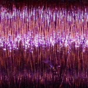 May include: Close-up of a spool of metallic purple thread. The thread has a shiny, iridescent finish.