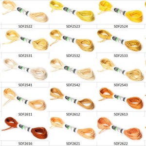 May include: A collection of twenty-five skeins of embroidery floss arranged in a grid, each featuring a unique shade of yellow, gold, or orange. Each skein is secured with a white paper label displaying a specific product code like SDF2521.