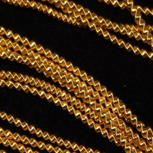 May include: Close-up of a gold chain with a twisted design. The chain is made of multiple strands of gold wire that are twisted together to create a rope-like effect.