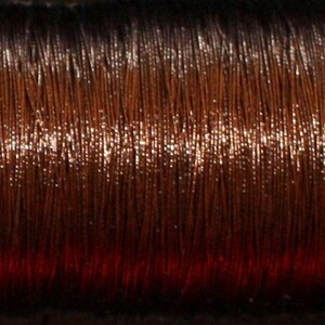 May include: A spool of brown metallic thread with a slight sheen. The thread is wound tightly and appears to be very fine.