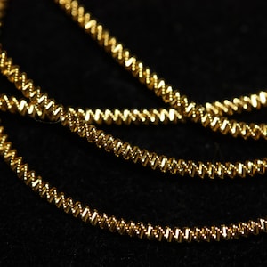 May include: Close-up of a gold chain necklace with a twisted design. The chain is made of small, round links that are twisted together to create a unique look.