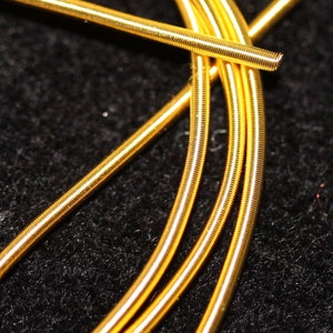 May include: Close-up of four gold-colored guitar strings wound together. The strings are coiled and have a shiny finish.