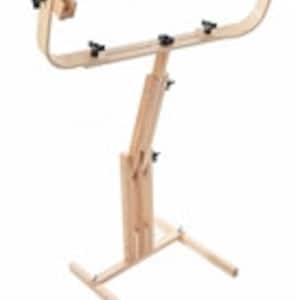 May include: A wooden, adjustable cross-stitch stand. The stand features a curved top frame with adjustable clamps, a central support column, and a base with two legs. The natural wood finish is visible throughout the stand.