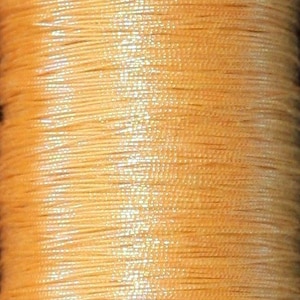 May include: A spool of light orange thread with a subtle shimmer.