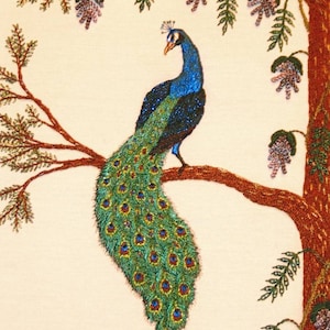 May include: Embroidered artwork of a peacock with a blue and green tail perched on a brown branch with purple flowers hanging from the branches.