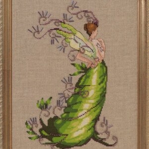 May include: A green fairy with wings and a flower crown is depicted in a cross-stitch pattern. The fairy is wearing a green dress and is surrounded by purple flowers.