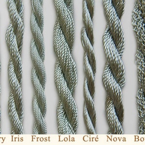 May include: Close-up of eight different types of silver-grey embroidery floss, including Glory, Iris, Frost, Lola, Cir&eacute;, Nova, and Boucl&eacute;.