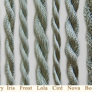 May include: Close-up of eight different types of silver-grey embroidery floss, including Glory, Iris, Frost, Lola, Cir&eacute;, Nova, and Boucl&eacute;.