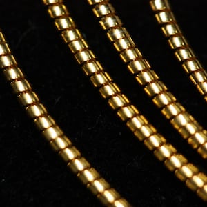 May include: Close-up of four gold-colored chains, each made of small, round links. The chains are arranged in a layered pattern, creating a textured and luxurious look.