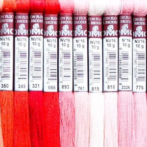May include: A collection of 20 DMC embroidery floss spools in various shades of yellow, orange, red, pink, and purple. Each spool is labeled with the DMC number and color name.