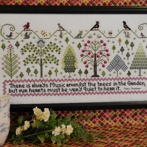 May include: Framed cross-stitch artwork featuring a garden scene with trees, birds, and the text "There is Always Music amongst the trees in the Garden, but our hearts must be very quiet to hear it." The frame is black.