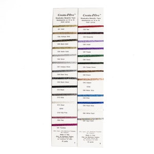 May include: A color chart of Cresta d'Oro Washable Metallic Yarn for needlepoint. The chart shows 21 different colors of yarn, including gold, silver, red, blue, green, and purple. Each color is labeled with a code and the yarn is wound around a card. The chart also includes information about the yarn, such as the composition and the length of the yarn. Made in Italy. Dist. by Rainbow Gallery.