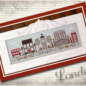 May include: Cross-stitch pattern featuring a red double-decker bus, a red telephone booth, and a clock tower with the word "London" in the center. The pattern is framed in a white frame with a red mat.