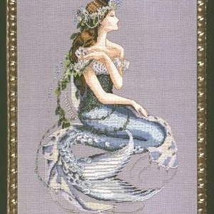 May include: A cross-stitch pattern of a mermaid with a blue tail and a crown of flowers on her head. She is sitting on a rock with her tail curled around her.