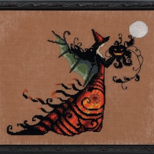 May include: Cross-stitch artwork of a witch holding a jack-o'-lantern and a moon. The witch wears a red hat, black dress, and green wings. The artwork is framed in a black frame and features orange, black, and brown colors.