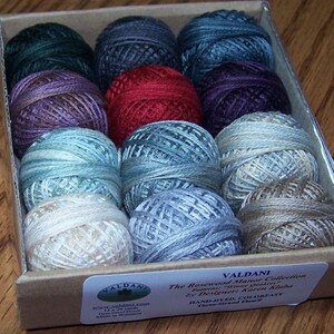May include: A selection of Valdani hand-dyed, colourfast thread balls in a range of hues, including green, blue, red, and purple. The Rosewood Manor Collection is designed by Karen Kluba. The box contains 12 x 26.5 m skeins.