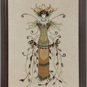 May include: A cross-stitch embroidery of a woman in a long, flowing gown with a leafy design. The gown is brown, green, and blue, and the woman has a crown of leaves on her head. The background is a light beige.