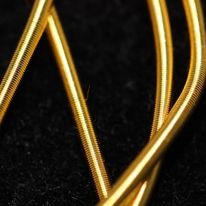 May include: Three gold-colored guitar strings wound together against a black background.