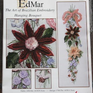 May include: A close-up of a cross-stitch embroidery pattern for a hanging bouquet of flowers. The pattern features a large red flower with green leaves, a pink bow, and a variety of other flowers in shades of pink, orange, and blue. The pattern is labeled "EdMar The Art of Brazilian Embroidery Hanging Bouquet #1607".