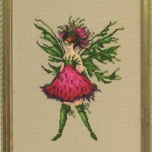 May include: A cross-stitch embroidery of a fairy with green wings and a pink dress. The fairy is wearing a mask and has a flower crown on her head.