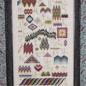 May include: A framed cross-stitch sampler with a white background and colorful embroidery of various stitches and letters. The sampler features a variety of geometric patterns and designs, including zigzags, diamonds, and stars.