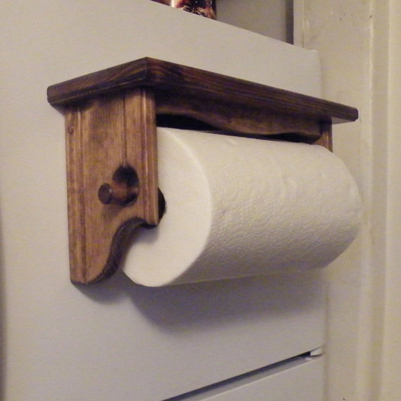 K&ouml;nnte beinhalten: Ein Holz-Papierrollenhalter mit einem Regal oben. Der Halter ist dunkelbraun gebeizt und hat ein schlichtes Design. Eine Rolle wei&szlig;er Papierhandt&uuml;cher befindet sich auf dem Halter.