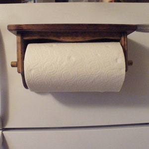 K&ouml;nnte beinhalten: Ein Holz-Papierrollenhalter, der an einem wei&szlig;en K&uuml;hlschrank befestigt ist. Der Halter hat ein Regal und eine Rolle Papierhandt&uuml;cher.