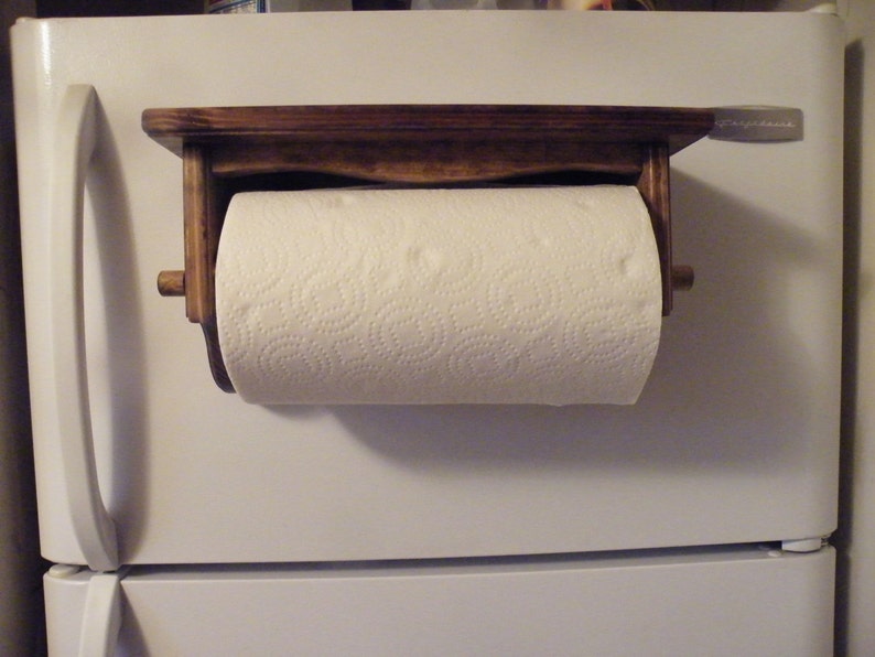 K&ouml;nnte beinhalten: Ein Holz-Papierrollenhalter, der an einem wei&szlig;en K&uuml;hlschrank befestigt ist. Der Halter hat ein Regal und eine Rolle Papierhandt&uuml;cher.
