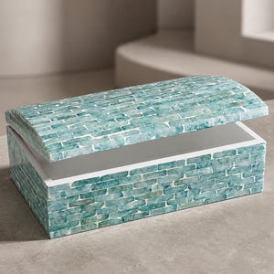 May include: A rectangular storage box with a hinged lid, featuring an exterior surface covered in small, teal and white brick-patterned tiles. The interior of the box is white, and the lid is slightly open, revealing the hollow storage compartment.
