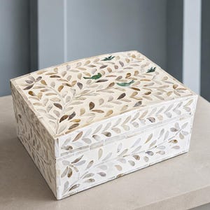 May include: A rectangular storage box featuring an intricate inlay pattern of white and tan leaf-shaped pieces. The design includes small green bird silhouettes integrated into the foliage motif across the lid and sides of the container.