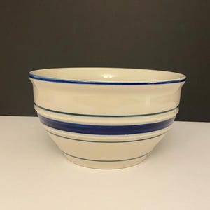 May include: A white ceramic bowl with blue and green stripes. The bowl is round and has a wide rim.