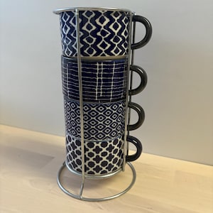 May include: A set of four blue and white ceramic mugs with geometric patterns, stacked on a metal stand.