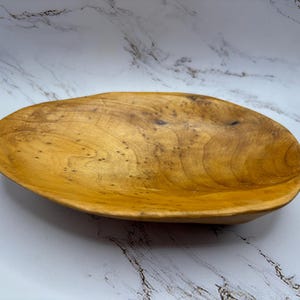 May include: A large, oval-shaped wooden serving bowl with a natural wood finish. The bowl is made of light brown wood with a smooth surface.