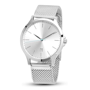 May include: A silver wristwatch with a mesh band. The watch has a round face with a silver dial, black hands, and a date window at the 6 o'clock position. The band is made of a fine, woven metal mesh. The watch is a classic, minimalist design.