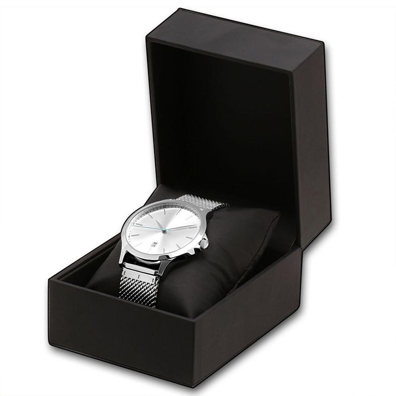 May include: A silver wristwatch with a mesh band rests on a black pillow inside an open black box. The watch has a silver face with blue hands and markers. The box is rectangular with a hinged lid.