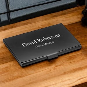 May include: Black metal business card holder with the name "David Robertson" and the title "General Manager" engraved in white.