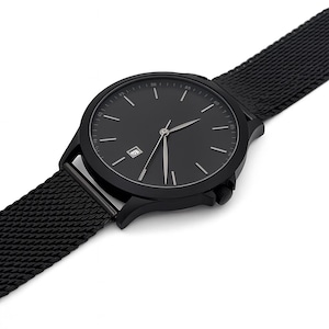 May include: A black wristwatch with a minimalist design. The watch features a round face with silver hands and markers, a date window, and a mesh band. The watch is angled, showing the details of the face and band.