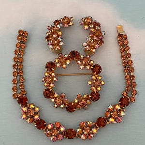 Könnte beinhalten: Ein Vintage-Schmuckset mit Armband, Ohrringen und Brosche. Das Set hat eine warme Farbpalette aus Orange und Braun mit funkelnden Strasssteinen. Armband und Ohrringe sind mit einer passenden Brosche verbunden.